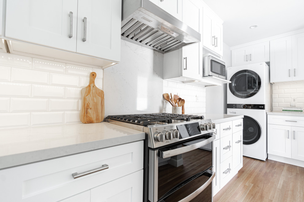 Foto på ett stort lantligt grå kök, med vita skåp, marmorbänkskiva, vitt stänkskydd, stänkskydd i tunnelbanekakel, rostfria vitvaror, målat trägolv och brunt golv