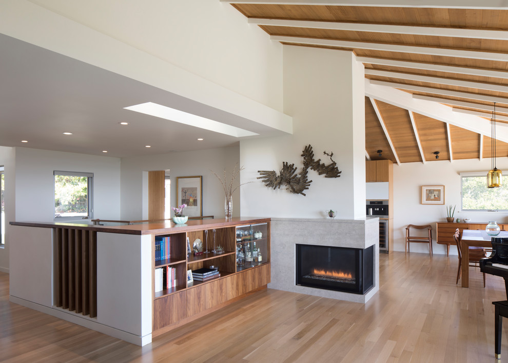 This is an example of a mid-sized modern loft-style living room in San Francisco with a library, white walls, medium hardwood floors, a corner fireplace, a stone fireplace surround and no tv.