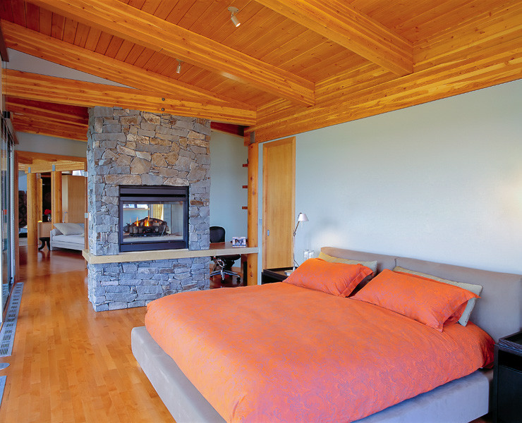 Inspiration for a large arts and crafts master bedroom in Denver with blue walls, light hardwood floors, a two-sided fireplace, a stone fireplace surround and brown floor.