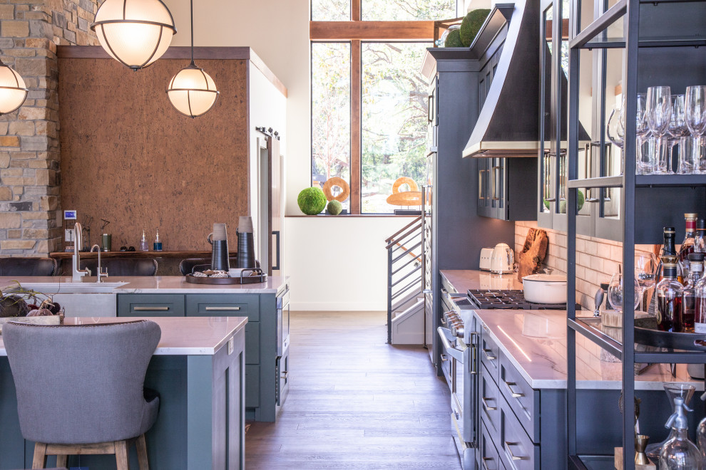 Inspiration for a large transitional u-shaped medium tone wood floor and brown floor open concept kitchen remodel with a farmhouse sink, shaker cabinets, black cabinets, quartzite countertops, white backsplash, porcelain backsplash, stainless steel appliances, two islands and white countertops