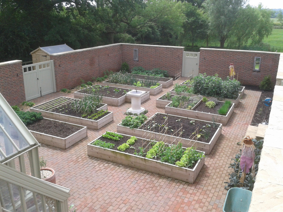 Large backyard formal garden in Gloucestershire with with raised garden bed and river rock.