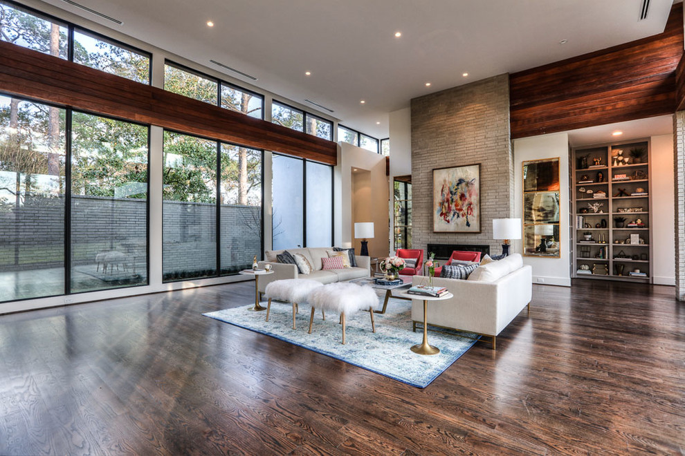 This is an example of an expansive contemporary formal open concept living room in Houston with white walls, dark hardwood floors, a hanging fireplace, a brick fireplace surround and no tv.
