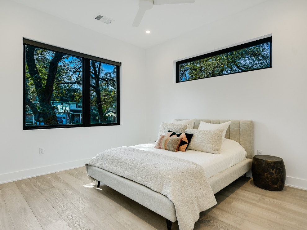 Photo of a large modern master bedroom in Austin with white walls and light hardwood floors.