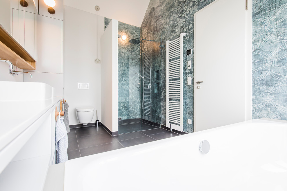 Photo of a mid-sized scandinavian 3/4 bathroom in Munich with open cabinets, white cabinets, a drop-in tub, a curbless shower, a two-piece toilet, white walls, cement tiles, a vessel sink, black floor, a hinged shower door and white benchtops.
