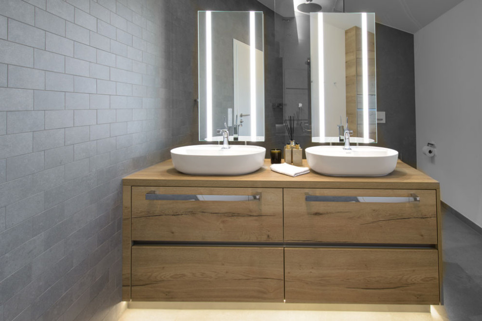 Photo of an industrial master bathroom in Dortmund with a curbless shower, a two-piece toilet, gray tile, ceramic tile, grey walls, ceramic floors, wood benchtops, grey floor, an open shower, brown benchtops, a double vanity and a freestanding vanity.