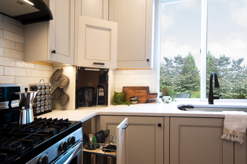 Mid-sized transitional l-shaped medium tone wood floor and brown floor kitchen photo with an undermount sink, recessed-panel cabinets, gray cabinets, quartz countertops, white backsplash, ceramic backsplash, stainless steel appliances, a peninsula and white countertops