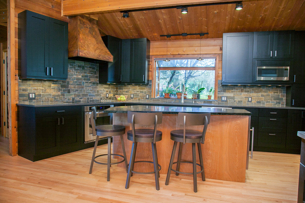 Inspiration for a large rustic l-shaped light wood floor and beige floor open concept kitchen remodel in Portland with shaker cabinets, black cabinets, stainless steel appliances, an island, an undermount sink, soapstone countertops, multicolored backsplash and stone tile backsplash
