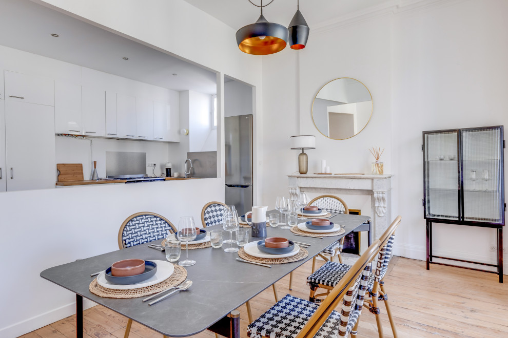 Idée de décoration pour une salle à manger ouverte sur la cuisine tradition avec un mur blanc, un sol en bois brun, une cheminée standard, un manteau de cheminée en pierre et un sol marron.