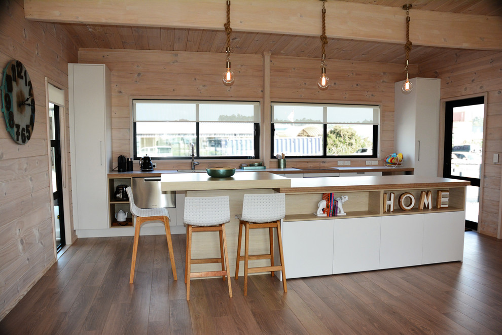 This is an example of a mid-sized modern galley eat-in kitchen in Auckland with a single-bowl sink, flat-panel cabinets, stainless steel appliances, laminate floors, with island, brown floor and beige benchtop.