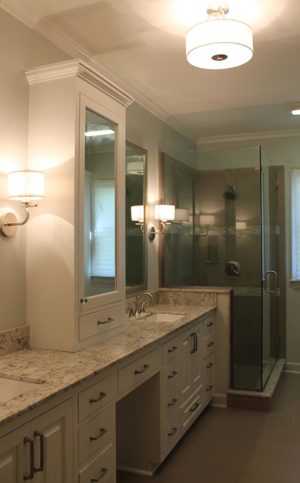 Design ideas for a mid-sized transitional bathroom in New Orleans with recessed-panel cabinets, white cabinets, granite benchtops, a drop-in tub, gray tile, porcelain tile, grey walls and porcelain floors.