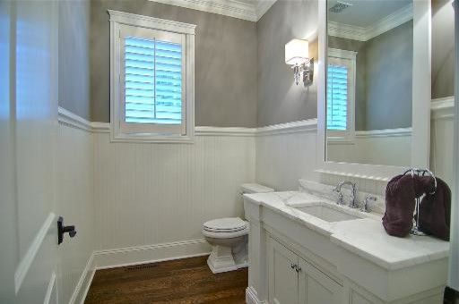 This is an example of a large traditional powder room in Chicago with recessed-panel cabinets, white cabinets, a one-piece toilet, grey walls, medium hardwood floors, an undermount sink, engineered quartz benchtops, gray tile, brown floor, white benchtops, a floating vanity and decorative wall panelling.