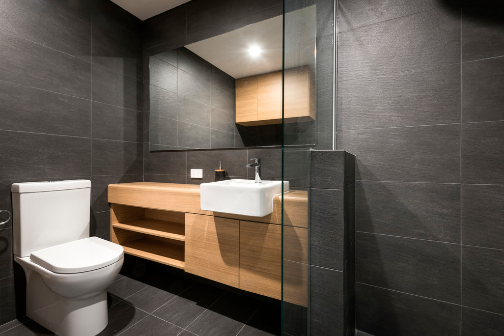 Photo of a mid-sized contemporary bathroom in Perth with light wood cabinets, a corner shower, black tile, ceramic tile, black walls, ceramic floors, laminate benchtops, flat-panel cabinets, a two-piece toilet, a drop-in sink, black floor and an open shower.