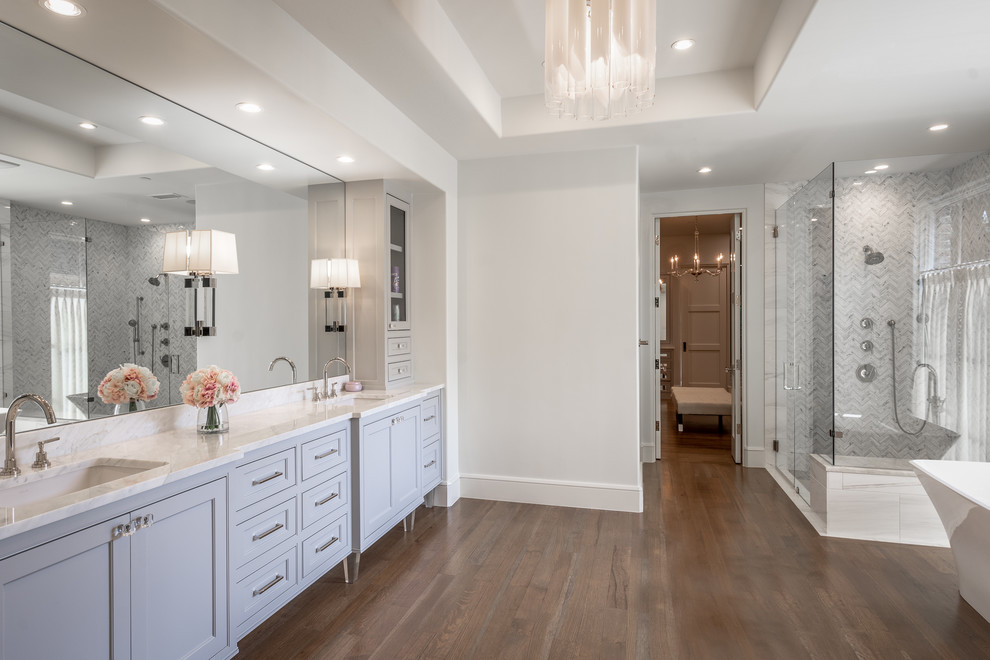 Inspiration for a transitional bathroom in Dallas with beaded inset cabinets, grey cabinets, a freestanding tub, white walls, dark hardwood floors, an undermount sink, brown floor and white benchtops.