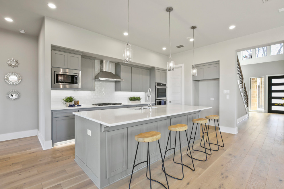 This is an example of a large traditional l-shaped open plan kitchen in Dallas with a submerged sink, beaded cabinets, grey cabinets, marble worktops, white splashback, ceramic splashback, stainless steel appliances, light hardwood flooring, an island, beige floors and white worktops.