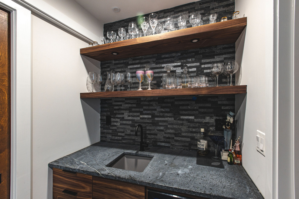 Inspiration for a small industrial single-wall wet bar in DC Metro with an undermount sink, flat-panel cabinets, dark wood cabinets, soapstone benchtops, grey splashback, stone tile splashback, concrete floors, grey floor and grey benchtop.