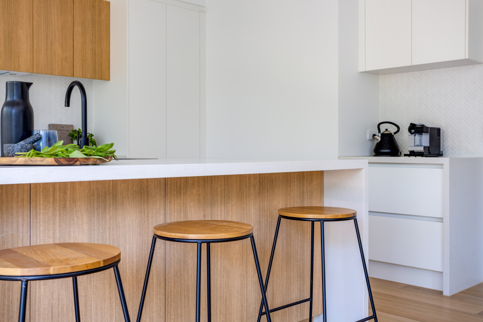 Inspiration for a large scandinavian u-shaped kitchen pantry in Melbourne with an undermount sink, recessed-panel cabinets, white cabinets, quartz benchtops, grey splashback, porcelain splashback, stainless steel appliances, medium hardwood floors, with island and white benchtop.