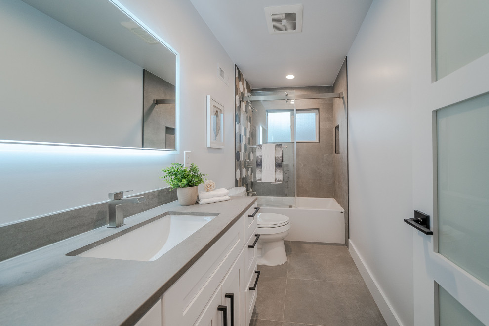 This is an example of a large contemporary family bathroom in San Francisco with shaker cabinets, white cabinets, a submerged bath, a shower/bath combination, a one-piece toilet, grey tiles, cement tiles, blue walls, cement flooring, a submerged sink, quartz worktops, grey floors, a sliding door, grey worktops, a wall niche, a single sink and a built in vanity unit.