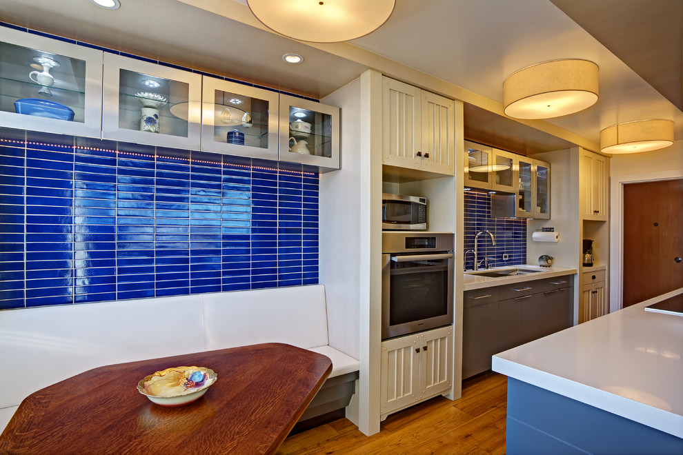 Photo of a small contemporary galley eat-in kitchen in San Francisco with an undermount sink, recessed-panel cabinets, beige cabinets, solid surface benchtops, blue splashback, ceramic splashback, stainless steel appliances, medium hardwood floors, a peninsula and yellow floor.