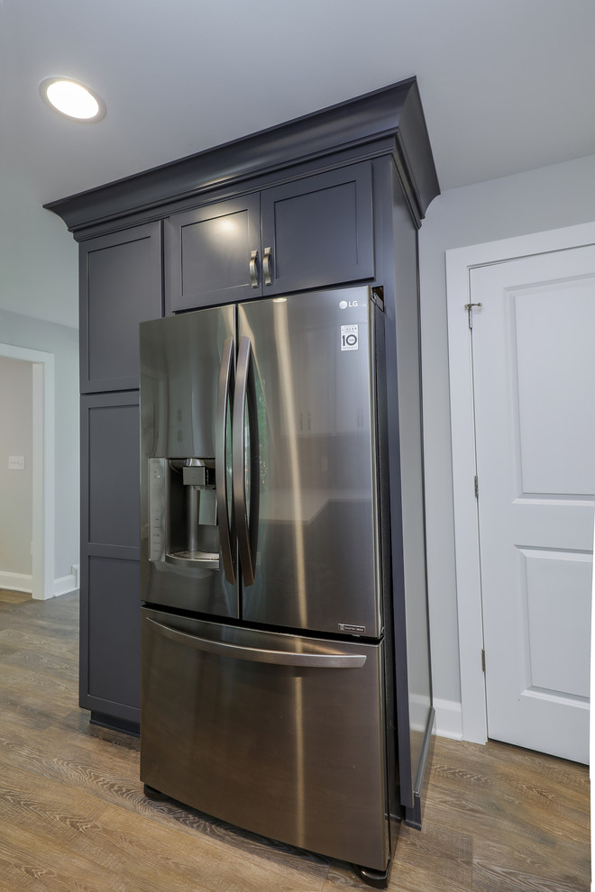 This is an example of a mid-sized traditional u-shaped separate kitchen in Cleveland with an undermount sink, shaker cabinets, grey cabinets, beige splashback, stainless steel appliances, medium hardwood floors, brown floor and white benchtop.