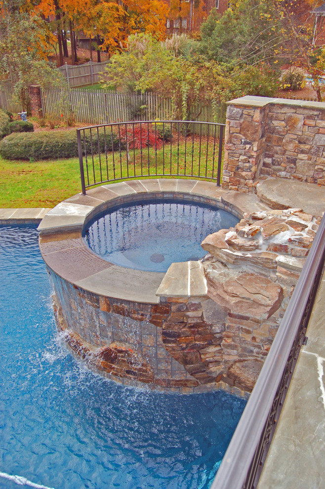 This is an example of a mid-sized country backyard custom-shaped natural pool in Charlotte with a hot tub and natural stone pavers.
