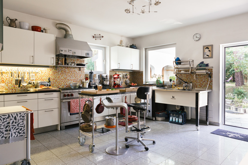 Large eclectic l-shaped open plan kitchen in Berlin with a double-bowl sink, flat-panel cabinets, white cabinets, multi-coloured splashback, mosaic tile splashback, stainless steel appliances and with island.