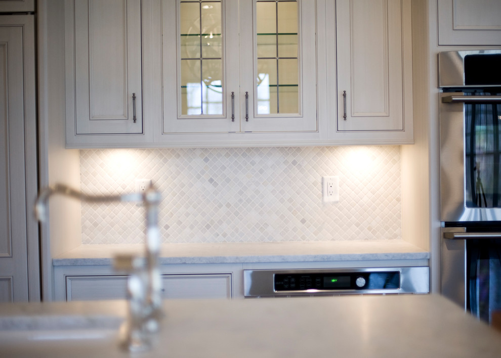 Transitional kitchen photo with an undermount sink, recessed-panel cabinets, white cabinets, marble countertops, white backsplash, mosaic tile backsplash, stainless steel appliances and an island