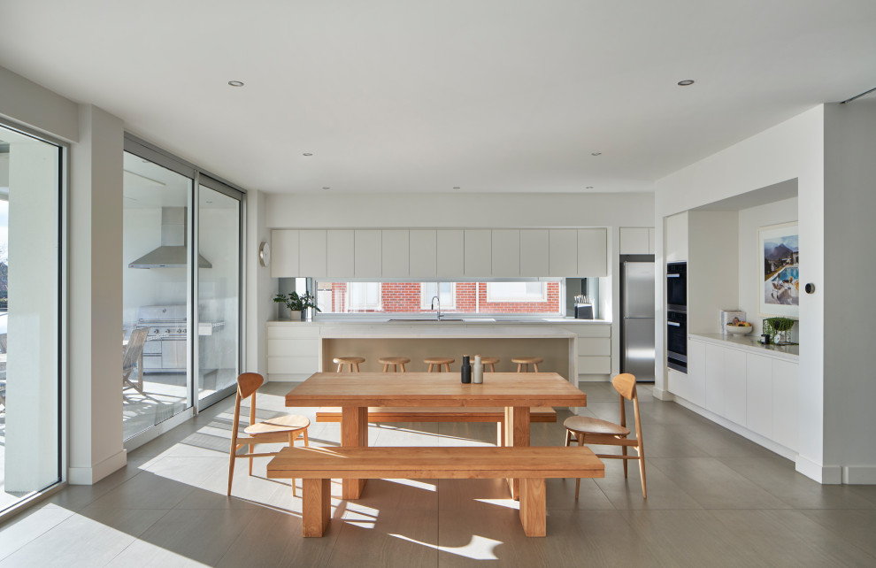 Large contemporary l-shaped open plan kitchen in Melbourne with a double-bowl sink, flat-panel cabinets, white cabinets, quartz benchtops, stainless steel appliances, with island and white benchtop.