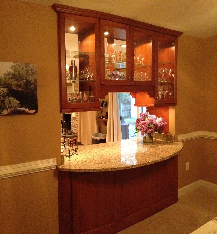 This is an example of a mid-sized transitional single-wall seated home bar in Baltimore with an undermount sink, glass-front cabinets, brown cabinets, granite benchtops, beige splashback, stone tile splashback and ceramic floors.