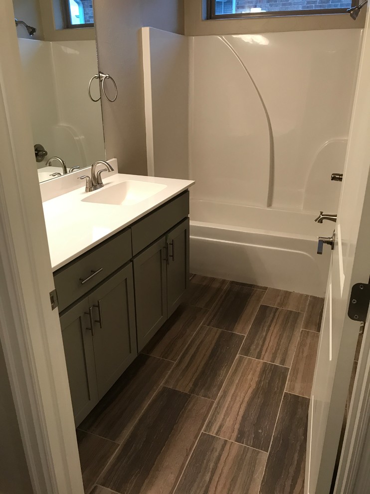Photo of a mid-sized transitional bathroom in Oklahoma City with shaker cabinets, grey cabinets, an alcove tub, a shower/bathtub combo, grey walls, ceramic floors, an integrated sink, solid surface benchtops and brown floor.