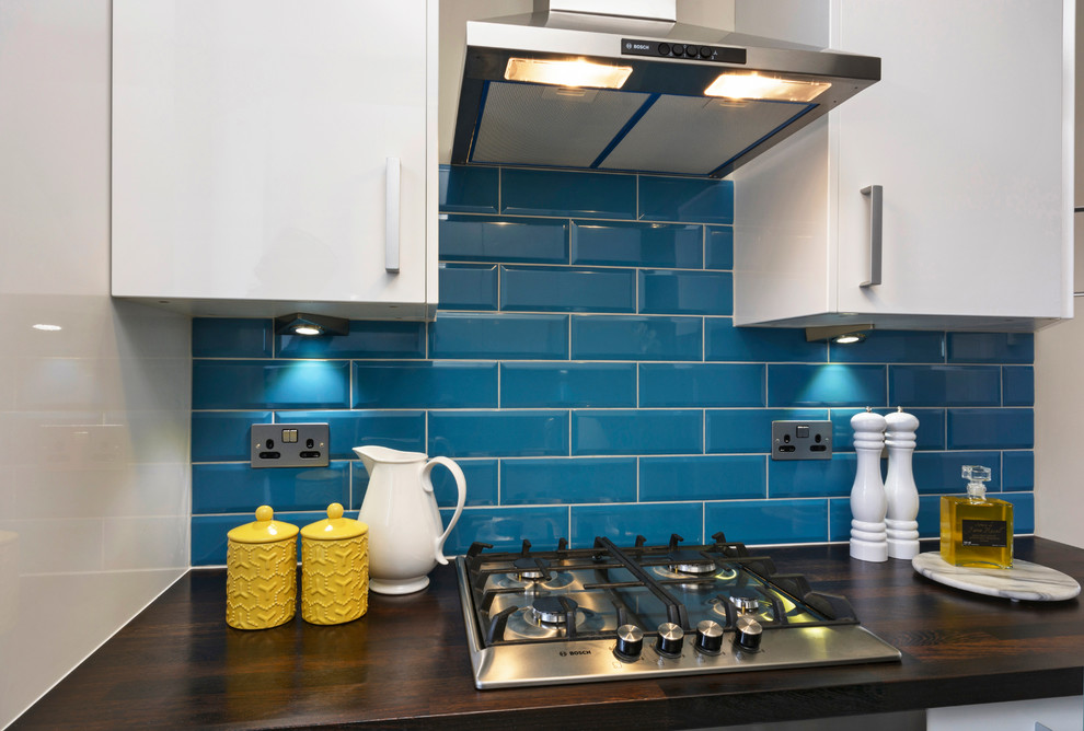 Small contemporary galley separate kitchen in London with an integrated sink, flat-panel cabinets, white cabinets, wood benchtops, blue splashback, ceramic splashback, stainless steel appliances, ceramic floors and no island.