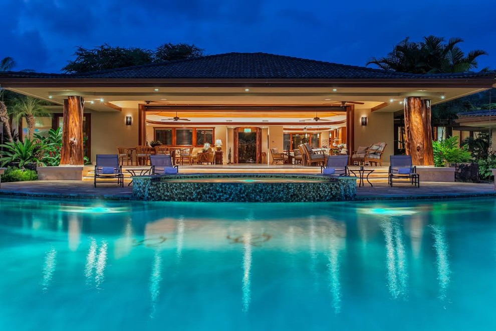 This is an example of a large tropical backyard custom-shaped infinity pool in Hawaii with a hot tub and natural stone pavers.