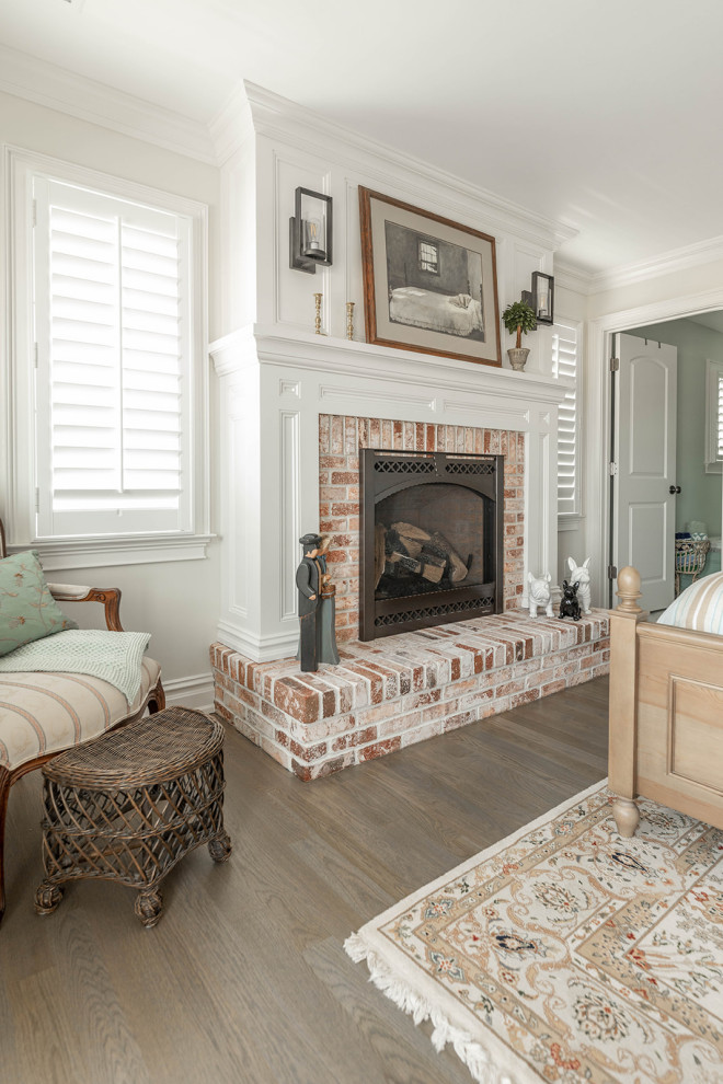 Cette photo montre une chambre parentale bord de mer avec un mur blanc, un sol en bois brun, une cheminée standard, un manteau de cheminée en brique et un sol marron.