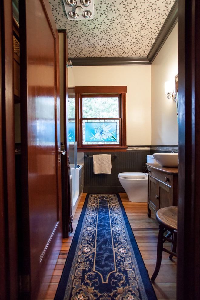 This is an example of a mid-sized country 3/4 bathroom in Seattle with dark wood cabinets, furniture-like cabinets, wood benchtops, brown benchtops, a shower/bathtub combo, a one-piece toilet, gray tile, matchstick tile, white walls, a vessel sink, a hinged shower door, a drop-in tub, medium hardwood floors and brown floor.