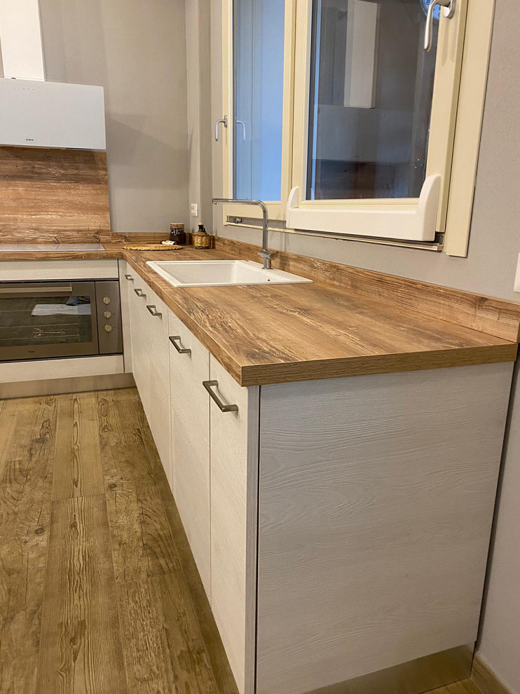 This is an example of a mid-sized scandinavian l-shaped eat-in kitchen in Other with a drop-in sink, light wood cabinets, laminate benchtops, stainless steel appliances, light hardwood floors, no island and exposed beam.