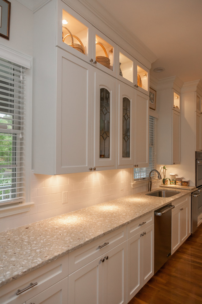 This is an example of an expansive traditional u-shaped eat-in kitchen in Charleston with with island, recessed-panel cabinets, white cabinets, recycled glass benchtops, an undermount sink, white splashback, ceramic splashback, stainless steel appliances and medium hardwood floors.