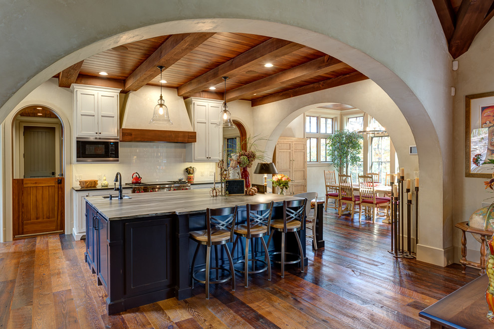 Large mountain style galley medium tone wood floor open concept kitchen photo with an undermount sink, shaker cabinets, white cabinets, marble countertops, white backsplash, subway tile backsplash, stainless steel appliances and an island