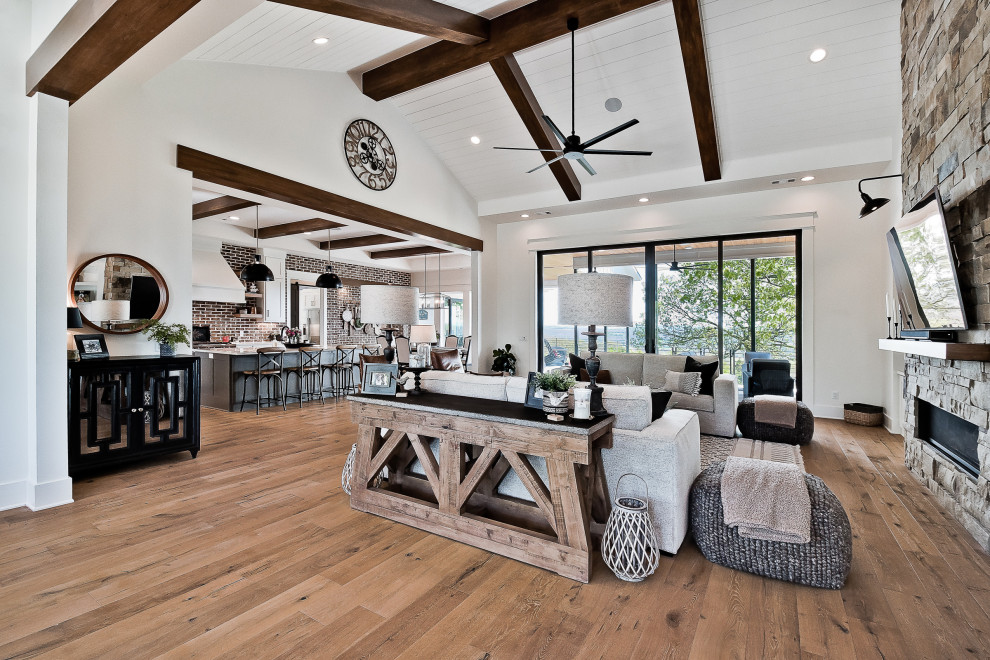 Inspiration for a large country open plan games room in Other with white walls, light hardwood flooring, a ribbon fireplace, a stone fireplace surround, a wall mounted tv and a vaulted ceiling.