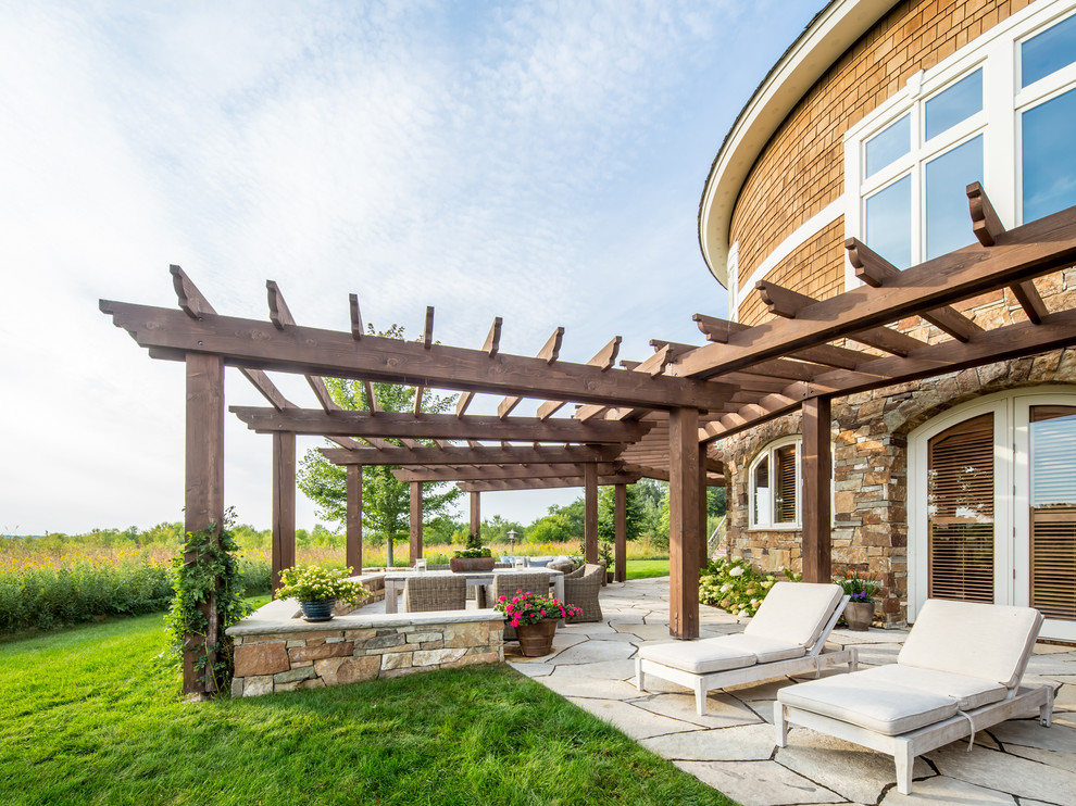 Large mountain style backyard stone patio photo in Minneapolis with a pergola