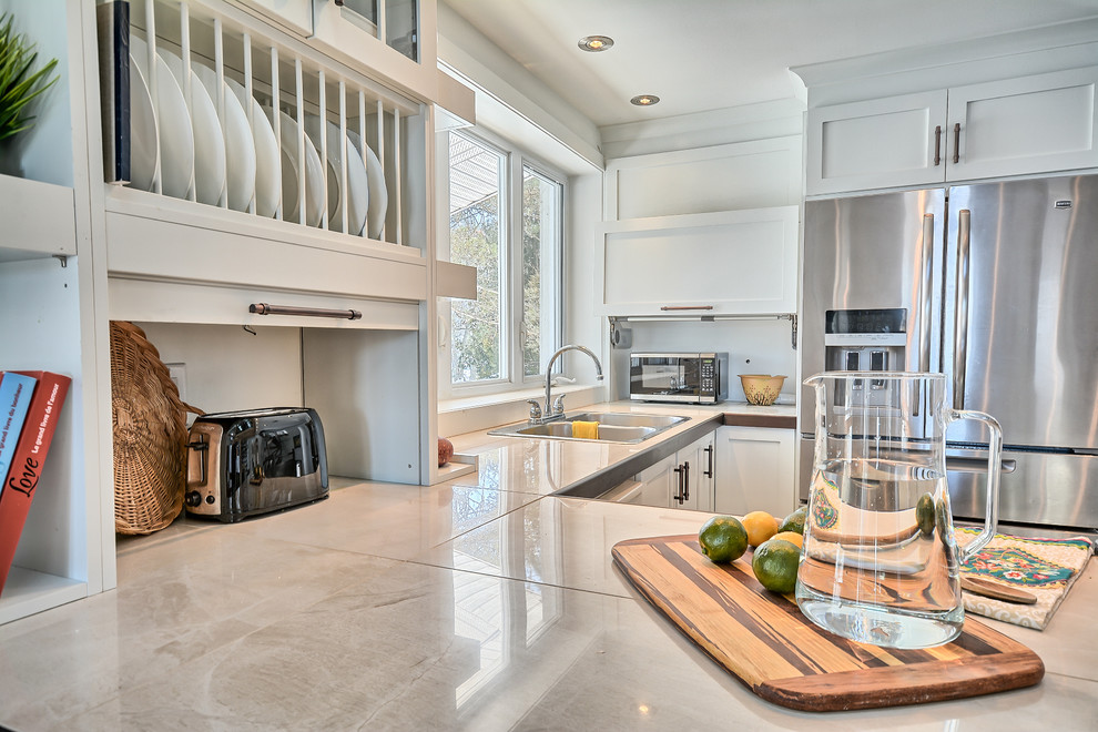 This is an example of a mid-sized eclectic u-shaped eat-in kitchen in Montreal with a double-bowl sink, shaker cabinets, white cabinets, tile benchtops, white splashback, window splashback, stainless steel appliances, slate floors and a peninsula.