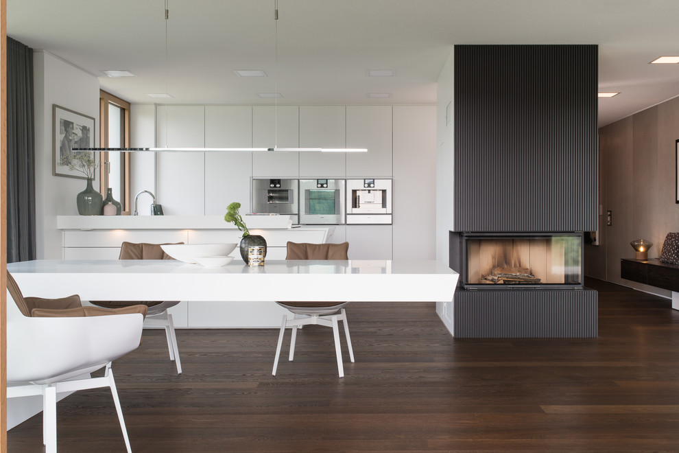 Inspiration for a large modern galley open plan kitchen in Stuttgart with flat-panel cabinets, white cabinets, stainless steel appliances, dark hardwood floors, brown floor, a peninsula and white benchtop.