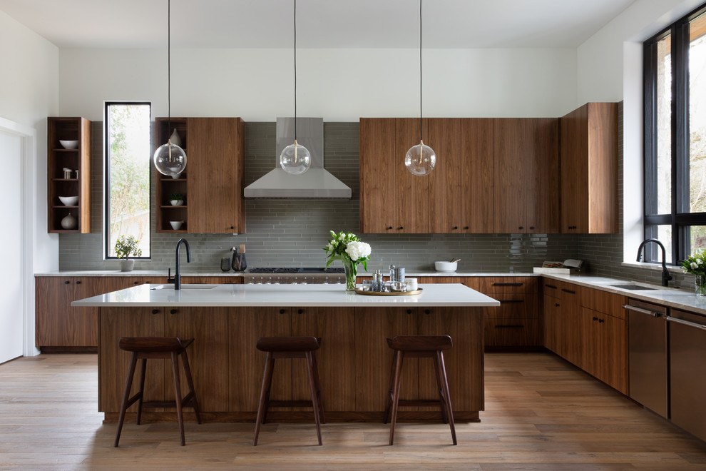 Photo of a contemporary l-shaped kitchen in Austin with an undermount sink, flat-panel cabinets, dark wood cabinets, grey splashback, stainless steel appliances, light hardwood floors, with island, beige floor and white benchtop.