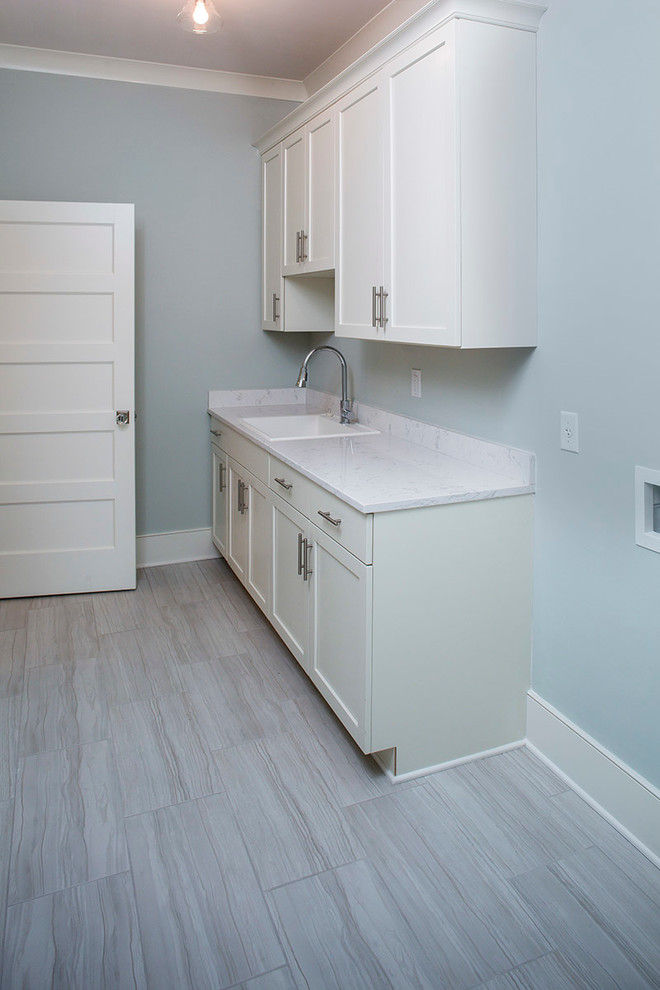 Design ideas for a mid-sized transitional single-wall dedicated laundry room in Charleston with a single-bowl sink, recessed-panel cabinets, white cabinets, solid surface benchtops, blue walls, porcelain floors and a side-by-side washer and dryer.