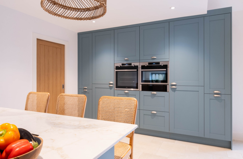 This is an example of a mid-sized contemporary eat-in kitchen in Gloucestershire with an integrated sink, shaker cabinets, blue cabinets, quartz benchtops, panelled appliances, porcelain floors, with island, beige floor and white benchtop.