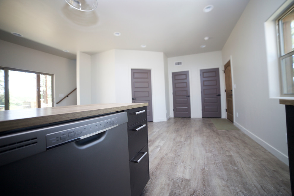 Example of a small mountain style medium tone wood floor open concept kitchen design in Phoenix with flat-panel cabinets, black cabinets, wood countertops and an island