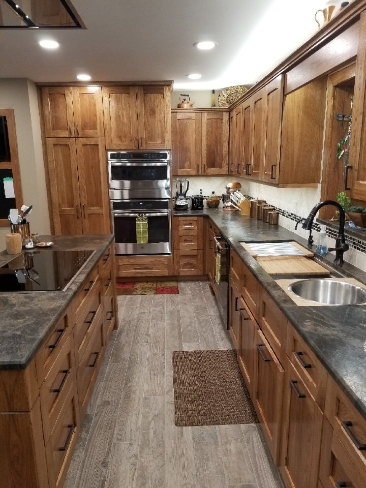This is an example of a mid-sized arts and crafts l-shaped eat-in kitchen in Other with an undermount sink, flat-panel cabinets, medium wood cabinets, granite benchtops, beige splashback, travertine splashback, stainless steel appliances, porcelain floors, with island, beige floor and black benchtop.