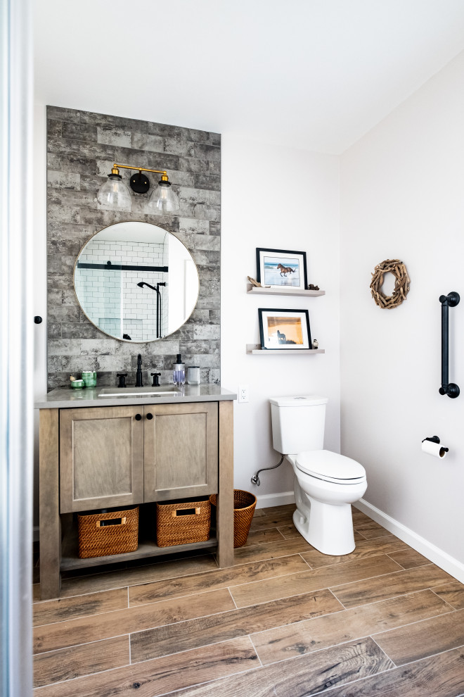 This is an example of a mid-sized country 3/4 bathroom in Newark with shaker cabinets, a two-piece toilet, gray tile, an undermount sink, engineered quartz benchtops, grey benchtops, a single vanity, medium wood cabinets, white walls, wood-look tile, brown floor and a freestanding vanity.