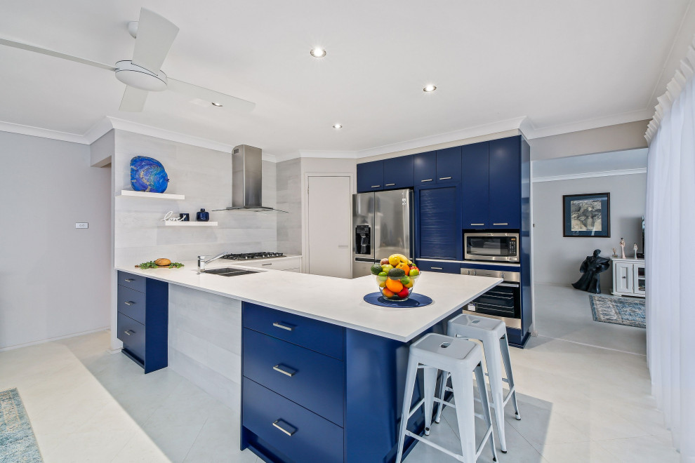 Photo of a mid-sized beach style u-shaped eat-in kitchen in Central Coast with an undermount sink, flat-panel cabinets, blue cabinets, solid surface benchtops, subway tile splashback, stainless steel appliances, cement tiles, a peninsula, white floor and white benchtop.