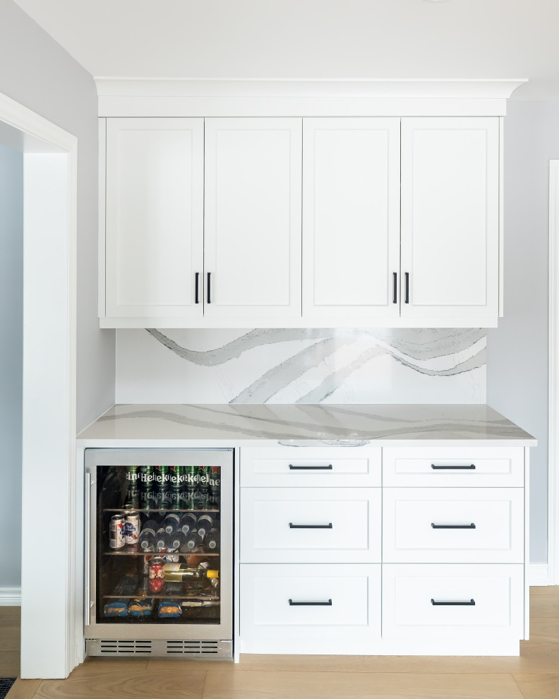 Inspiration for a mid-sized transitional u-shaped light wood floor eat-in kitchen remodel in Toronto with an undermount sink, shaker cabinets, white cabinets, quartz countertops, white backsplash, quartz backsplash, stainless steel appliances, an island and white countertops