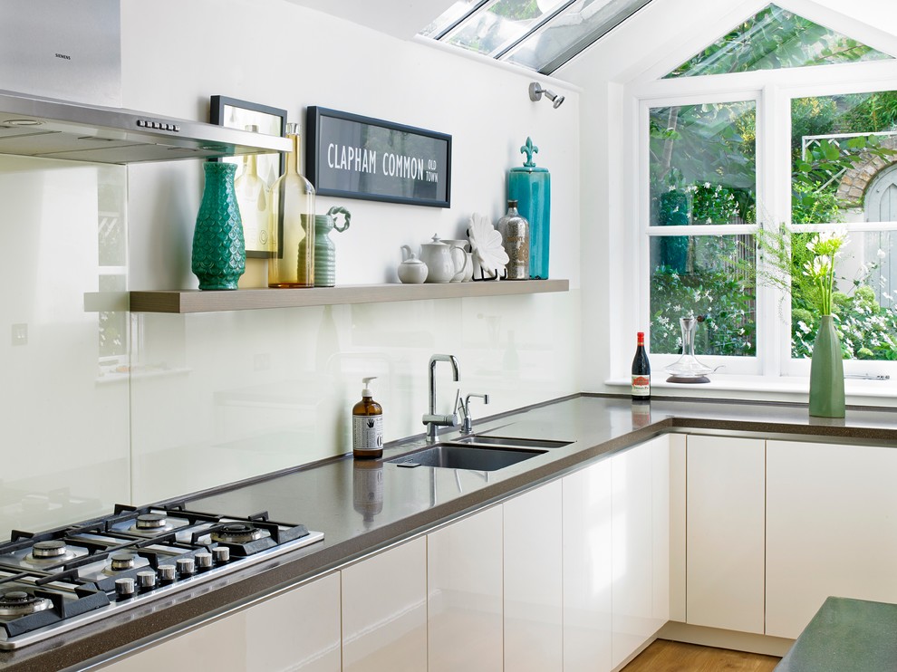 This is an example of a contemporary l-shaped kitchen in London with an undermount sink, flat-panel cabinets, white cabinets, white splashback and glass sheet splashback.