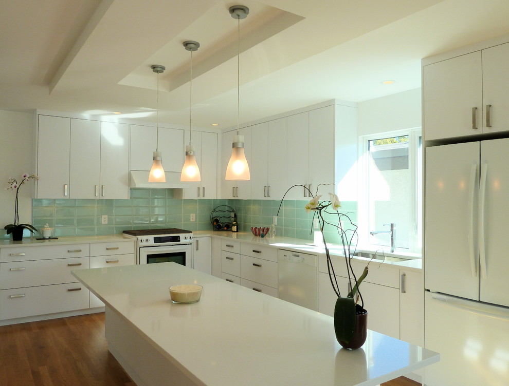 Photo of a modern l-shaped kitchen in Vancouver with white appliances, a single-bowl sink, white cabinets, blue splashback and subway tile splashback.